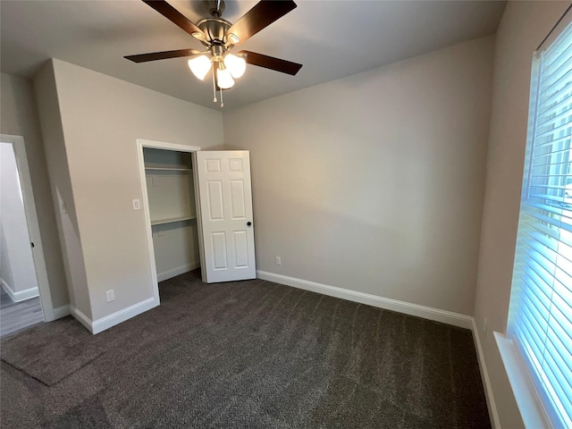 unfurnished bedroom featuring ceiling fan, a closet, multiple windows, and dark colored carpet