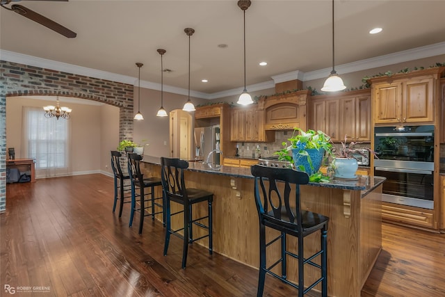 kitchen with pendant lighting, appliances with stainless steel finishes, dark stone countertops, a kitchen breakfast bar, and a spacious island