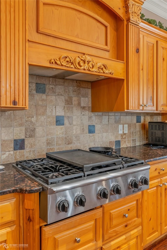 kitchen featuring stainless steel gas cooktop, ornamental molding, custom range hood, dark stone counters, and decorative backsplash