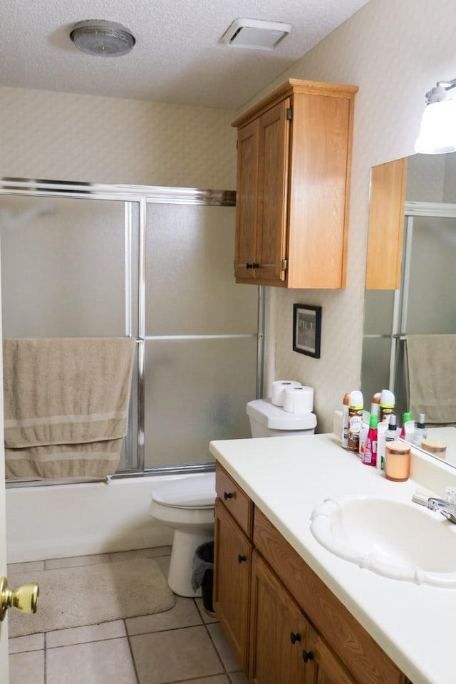 full bathroom with a textured ceiling, tile patterned floors, vanity, bath / shower combo with glass door, and toilet