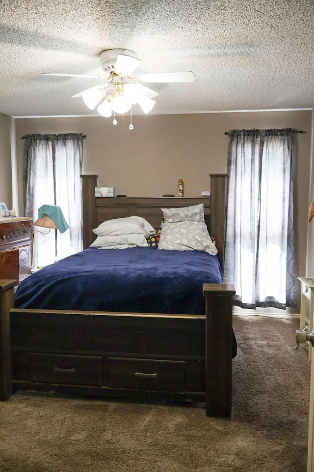 bedroom featuring ceiling fan, multiple windows, a textured ceiling, and dark colored carpet