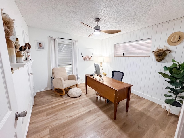 office area featuring a textured ceiling, ceiling fan, light hardwood / wood-style floors, and wood walls