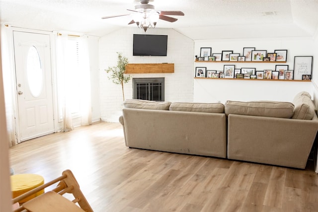 living room with lofted ceiling, ceiling fan, a brick fireplace, light hardwood / wood-style floors, and a textured ceiling