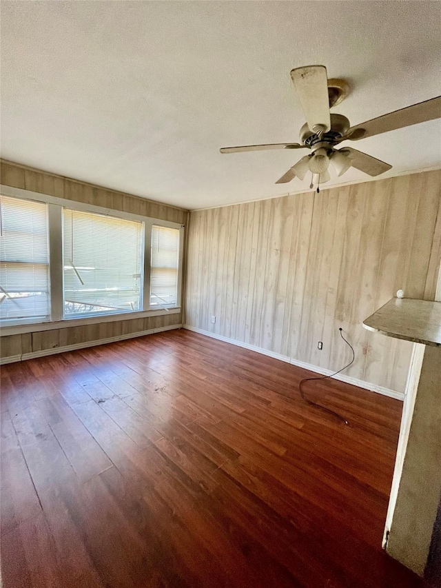 interior space featuring a textured ceiling, dark wood-type flooring, wooden walls, and ceiling fan