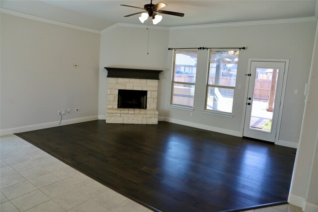 unfurnished living room with light tile patterned floors, a stone fireplace, ceiling fan with notable chandelier, baseboards, and crown molding