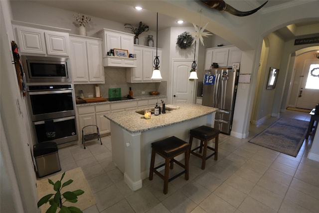 kitchen with light stone countertops, appliances with stainless steel finishes, white cabinetry, an island with sink, and light tile patterned floors