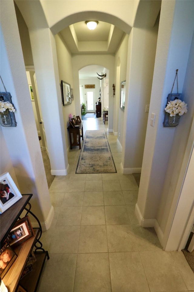 hallway with a raised ceiling and light tile patterned flooring