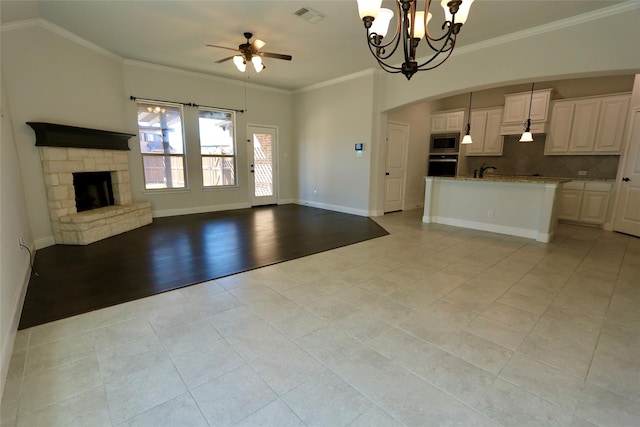 unfurnished living room featuring baseboards, visible vents, crown molding, a fireplace, and ceiling fan with notable chandelier