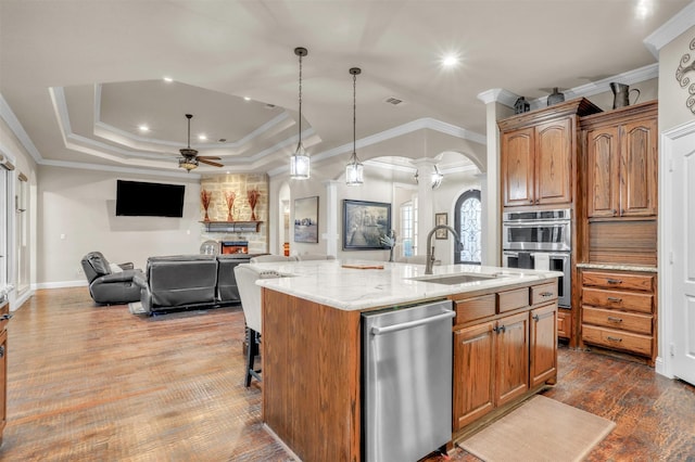 kitchen featuring an island with sink, sink, decorative columns, a tray ceiling, and crown molding