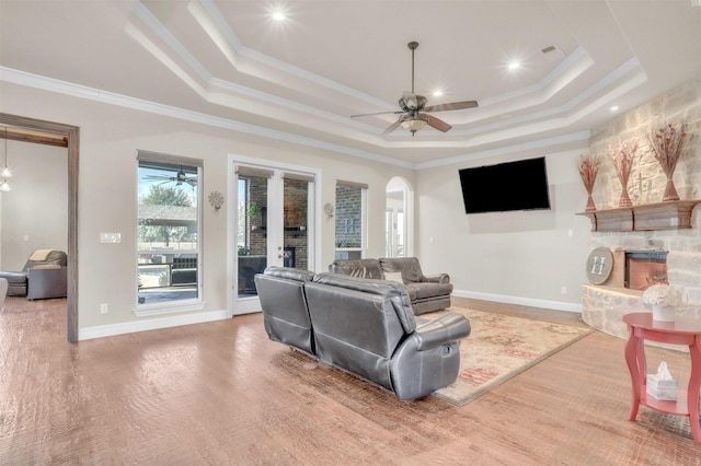 living room with ceiling fan, a fireplace, crown molding, a tray ceiling, and hardwood / wood-style flooring