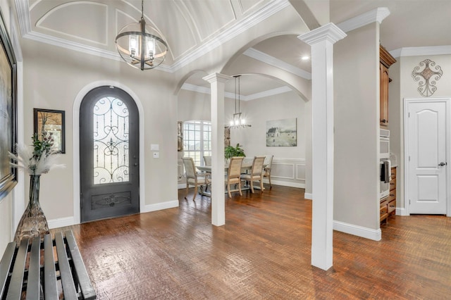 foyer with crown molding, dark wood-type flooring, an inviting chandelier, and ornate columns