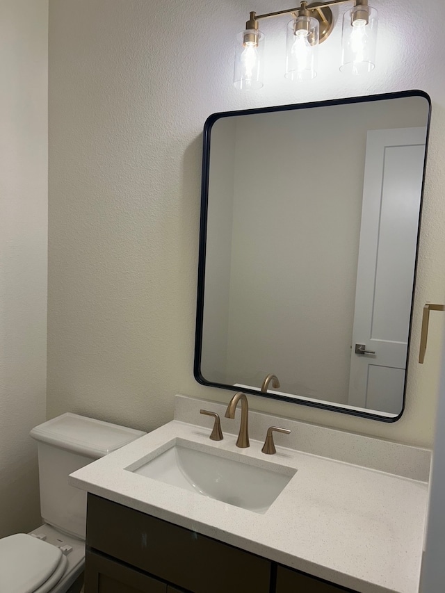 half bathroom with a textured wall, vanity, and toilet