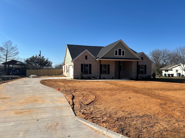 view of front of home featuring covered porch, brick siding, and fence