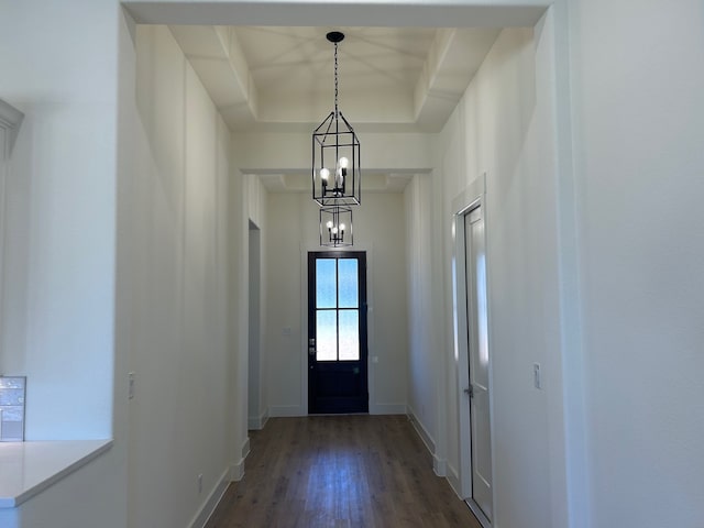 doorway featuring dark wood-style floors, a raised ceiling, a chandelier, and baseboards