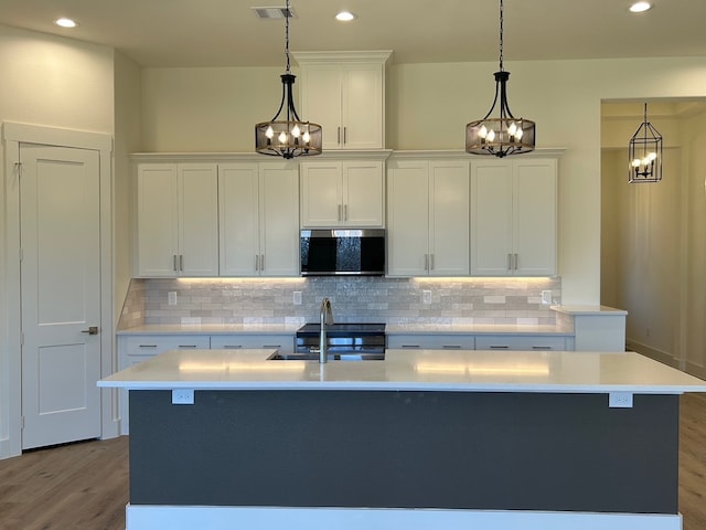 kitchen with stainless steel microwave, light wood-style flooring, an inviting chandelier, white cabinetry, and a sink