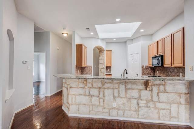 kitchen with a skylight, backsplash, kitchen peninsula, and light stone countertops