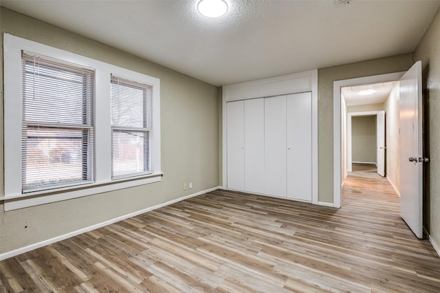 unfurnished bedroom with light wood-type flooring, a closet, and a textured ceiling