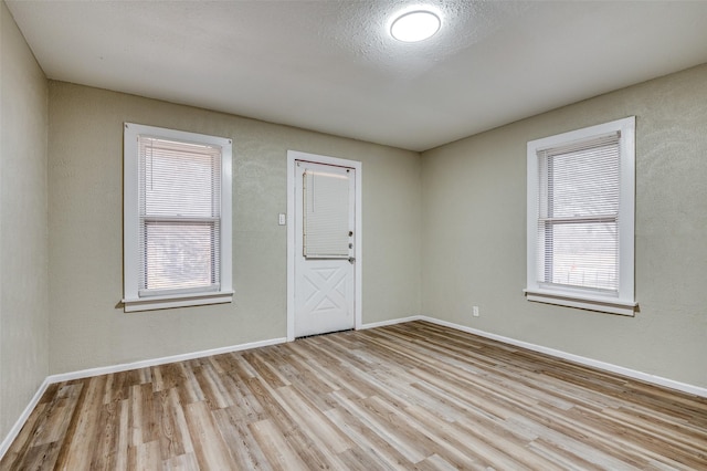 unfurnished room with a textured ceiling and light wood-type flooring