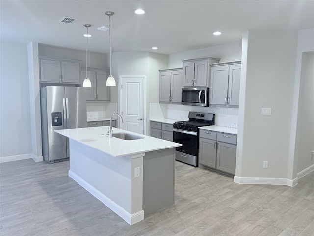 kitchen with sink, a kitchen island with sink, pendant lighting, stainless steel appliances, and light hardwood / wood-style floors