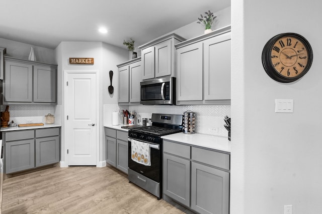 kitchen with backsplash, gray cabinets, light hardwood / wood-style floors, and appliances with stainless steel finishes