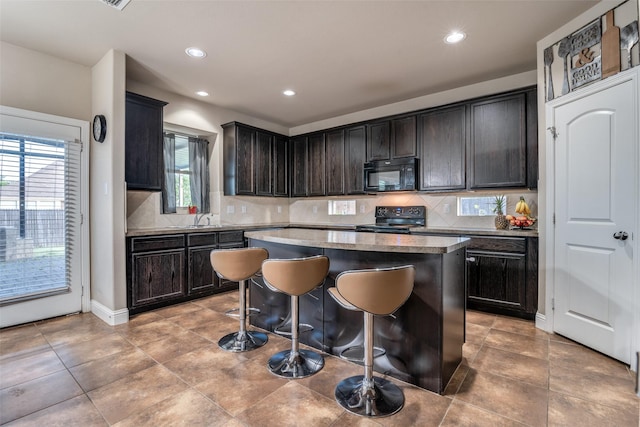 kitchen featuring dark brown cabinetry, a breakfast bar area, a kitchen island, decorative backsplash, and black appliances