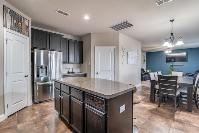 kitchen with stainless steel refrigerator with ice dispenser, dark brown cabinetry, decorative light fixtures, a chandelier, and a kitchen island