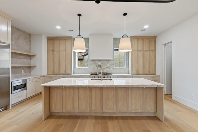 kitchen with decorative backsplash, an island with sink, light stone counters, and light hardwood / wood-style floors