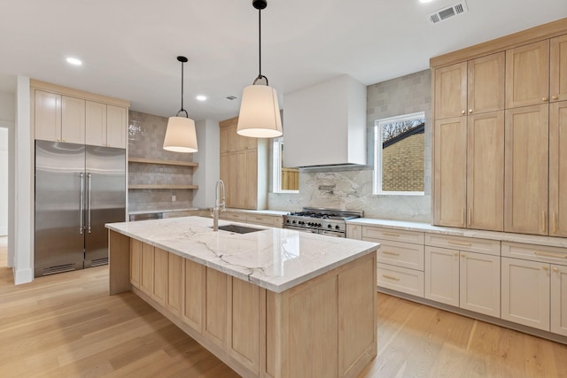 kitchen featuring decorative light fixtures, wall chimney range hood, high end appliances, sink, and a center island with sink