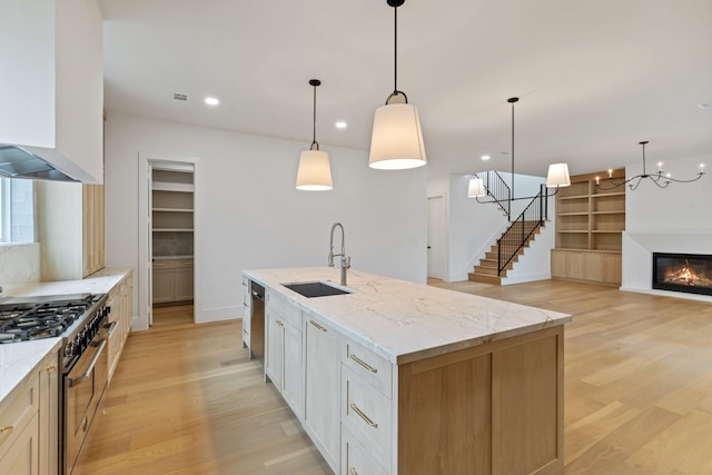 kitchen with decorative light fixtures, sink, appliances with stainless steel finishes, and a kitchen island with sink