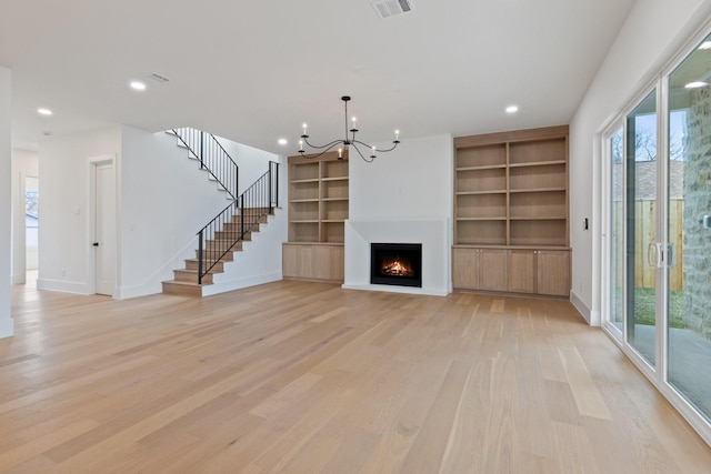 unfurnished living room featuring an inviting chandelier, light hardwood / wood-style floors, and built in shelves