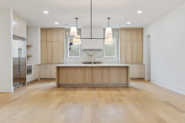 kitchen with built in fridge, decorative light fixtures, light brown cabinets, and a center island with sink