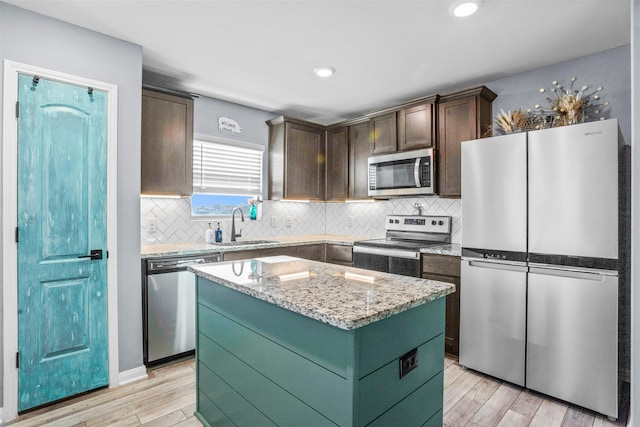 kitchen with a center island, sink, dark brown cabinetry, light stone countertops, and stainless steel appliances