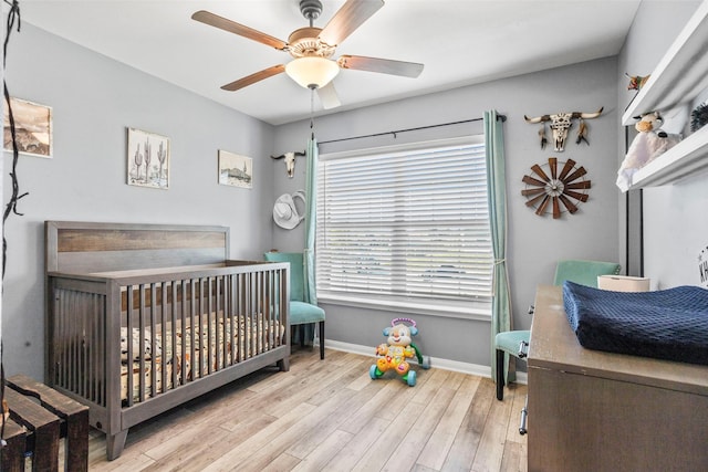 bedroom featuring ceiling fan, multiple windows, light hardwood / wood-style flooring, and a crib