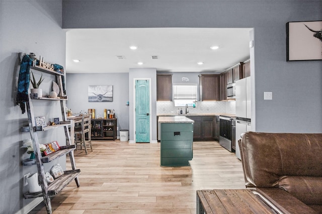 kitchen featuring appliances with stainless steel finishes, tasteful backsplash, light wood-type flooring, dark brown cabinetry, and a center island