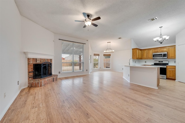 kitchen featuring ceiling fan with notable chandelier, appliances with stainless steel finishes, lofted ceiling, a brick fireplace, and light hardwood / wood-style flooring