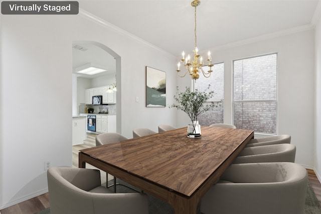 dining area with wood-type flooring, ornamental molding, and a chandelier