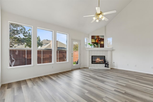 unfurnished living room with high vaulted ceiling, light hardwood / wood-style flooring, a tile fireplace, and ceiling fan