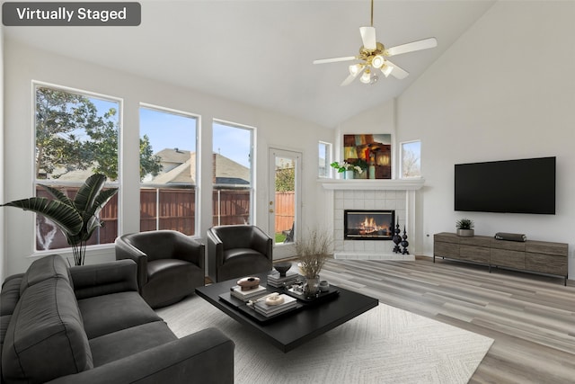 living room featuring high vaulted ceiling, light hardwood / wood-style flooring, a tile fireplace, and ceiling fan