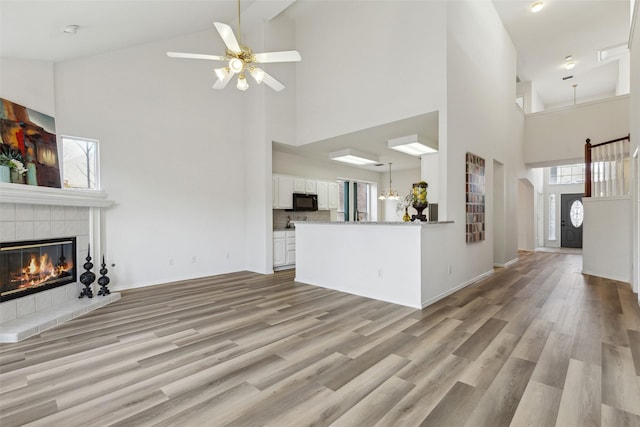 unfurnished living room featuring a tile fireplace, light wood-type flooring, and high vaulted ceiling