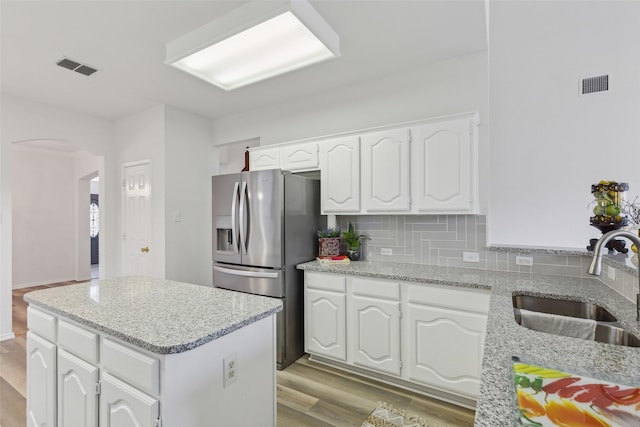 kitchen featuring sink, light stone counters, stainless steel fridge, white cabinets, and backsplash