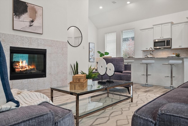 living room featuring lofted ceiling, sink, a fireplace, and light wood-type flooring