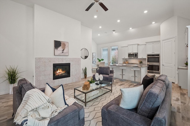 living room with ceiling fan, high vaulted ceiling, a fireplace, and light hardwood / wood-style flooring