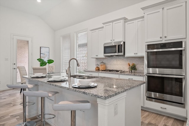 kitchen featuring sink, white cabinetry, appliances with stainless steel finishes, an island with sink, and light stone countertops