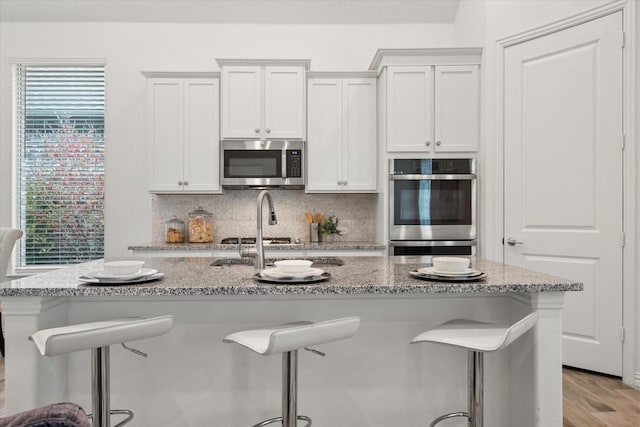 kitchen featuring a breakfast bar area, stainless steel appliances, light stone countertops, white cabinets, and decorative backsplash