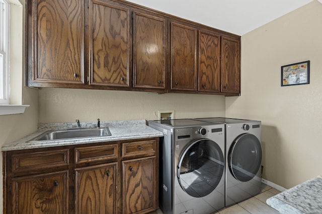 clothes washing area featuring light tile patterned floors, cabinet space, a sink, separate washer and dryer, and baseboards