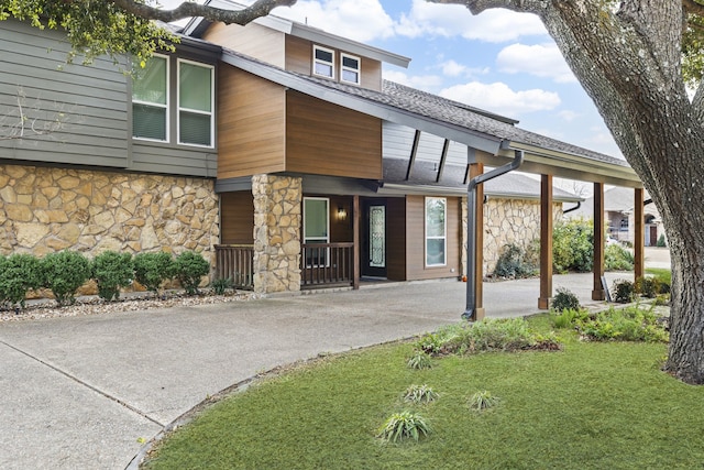 view of front of property with stone siding, a front lawn, aphalt driveway, and roof with shingles