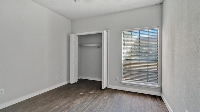 unfurnished bedroom featuring dark wood-type flooring, a textured ceiling, and a closet