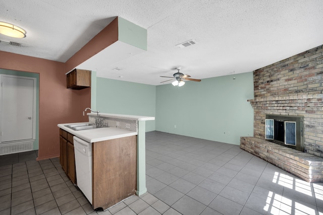 kitchen with ceiling fan, a brick fireplace, sink, white dishwasher, and a textured ceiling