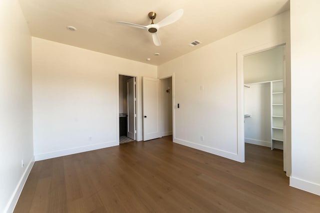 unfurnished bedroom with a closet, a walk in closet, dark hardwood / wood-style floors, and ceiling fan