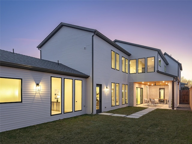 back house at dusk featuring a yard and a patio area